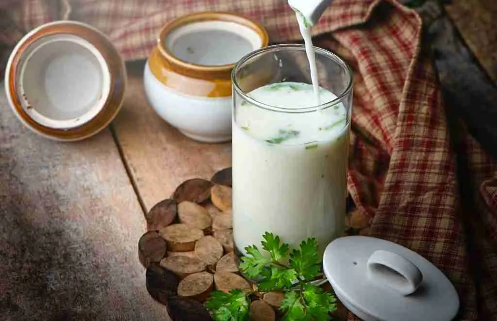Buttermilk in clear drinking glass with green leaves and white cream