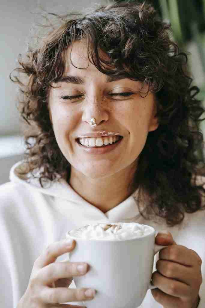 Cheerful woman with cream on nose and cup of coffee