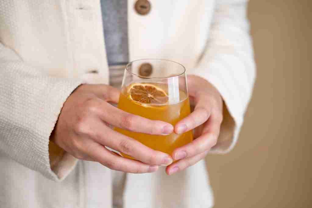 person holding clear Kombucha drink glass with orange liquid