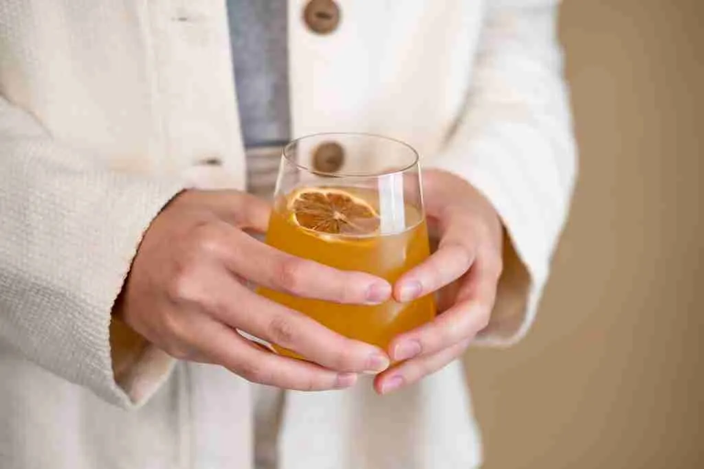 person holding clear Kombucha drink glass with orange liquid