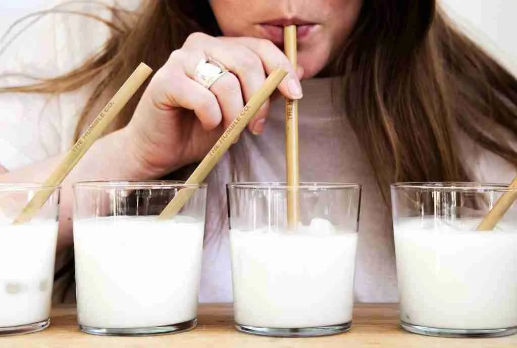woman holding brown wooden straw drinking milk