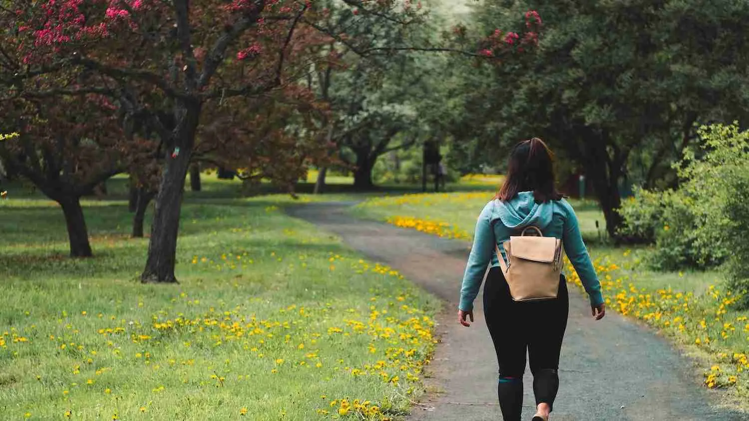 woman wearing blue jacket and black pants walking on grass field pathway