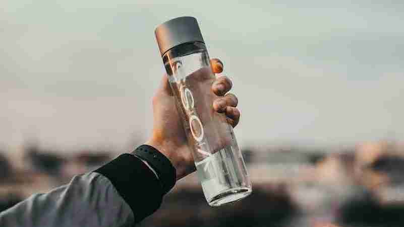 person holding clear glass mineral water bottle