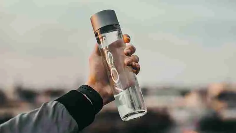 person holding clear glass mineral water bottle