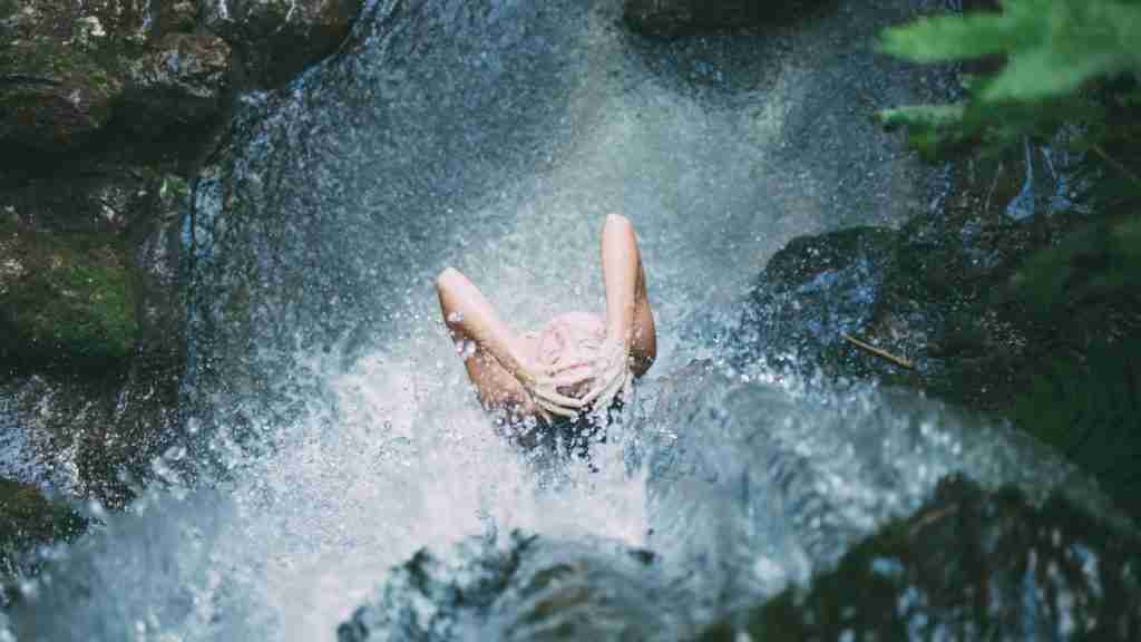high-angle photography of woman bathing below waterfalls during daytime