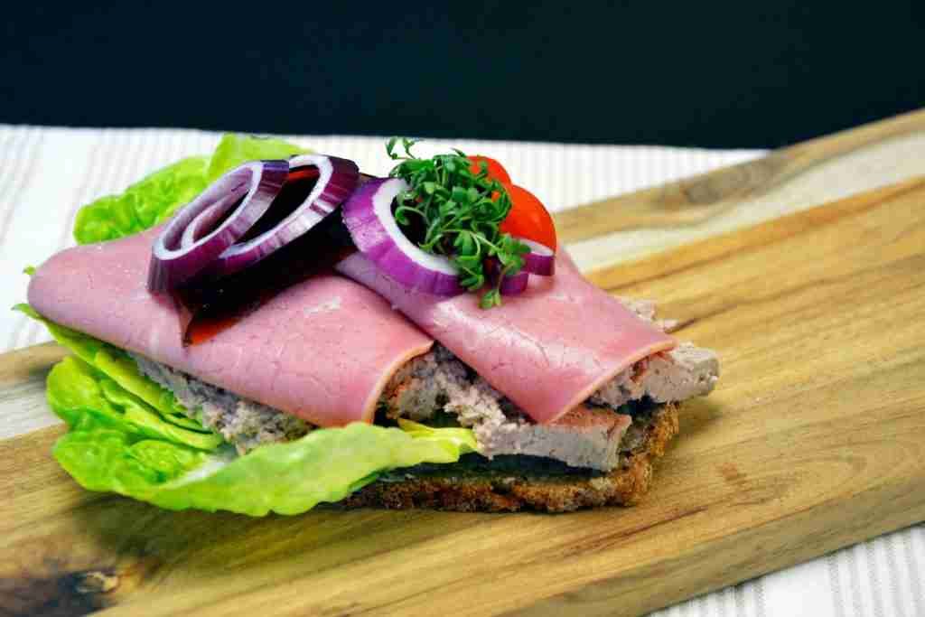 Rye bread ham sandwich with lettuce and tomato on brown wooden chopping board