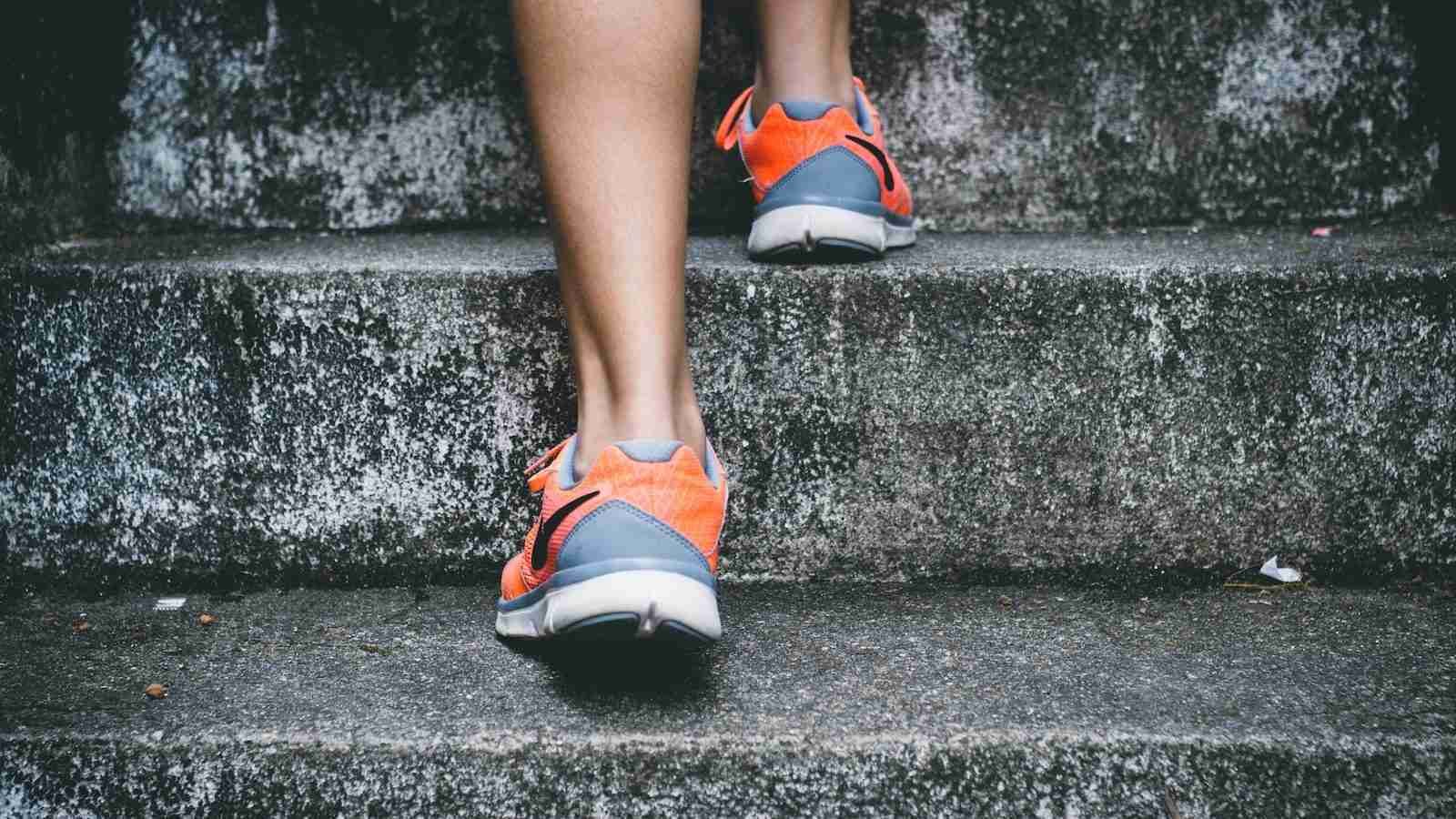 person wearing orange and gray Nike shoes walking on gray concrete stairs