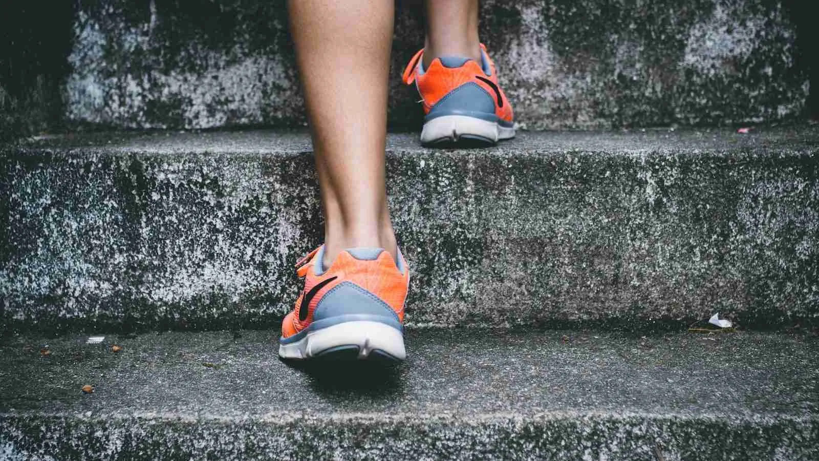 person wearing orange and gray Nike shoes walking on gray concrete stairs