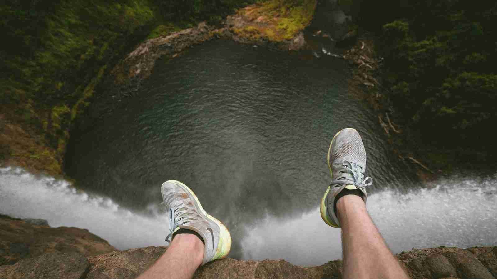 person sitting on edge of mountain overlooking lake during daytime