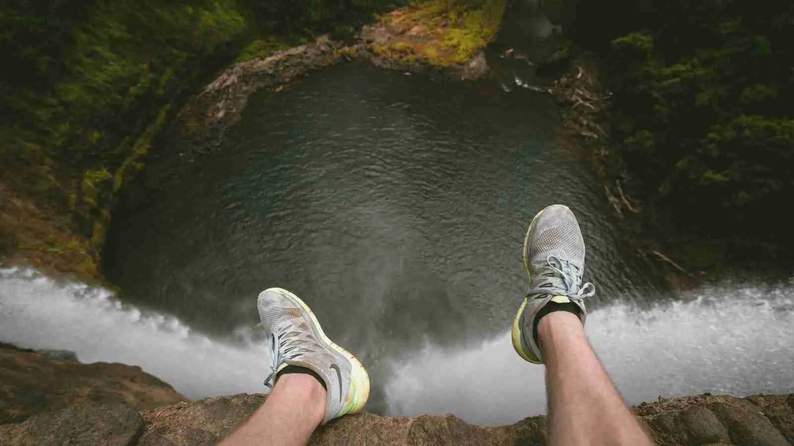 person sitting on edge of mountain overlooking lake during daytime