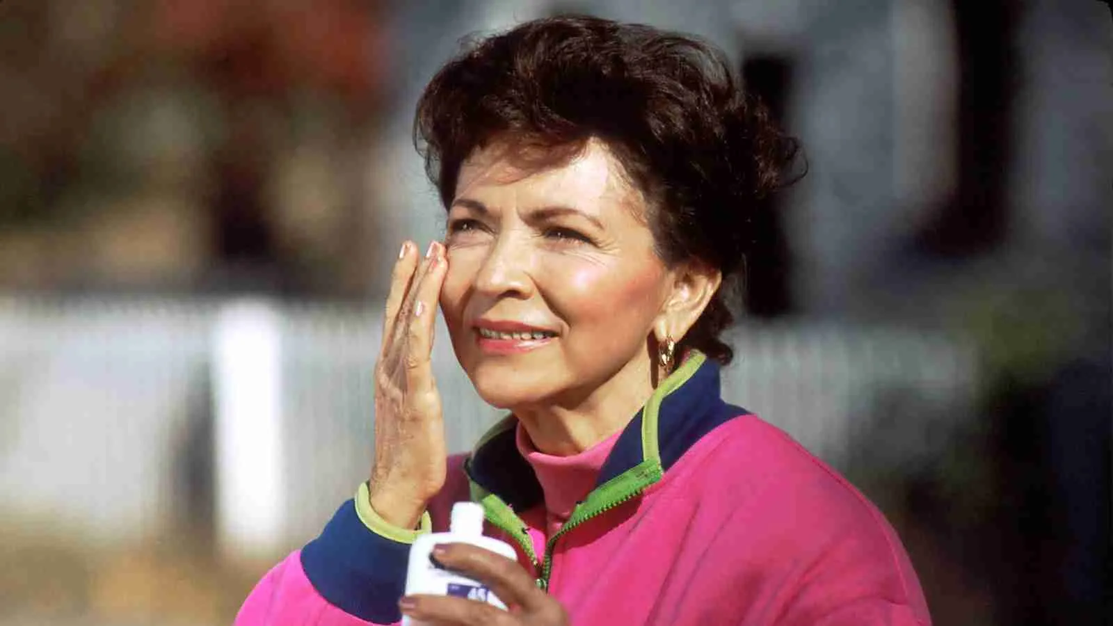 smiling woman in pink and blue shirt applying sun screen on her face