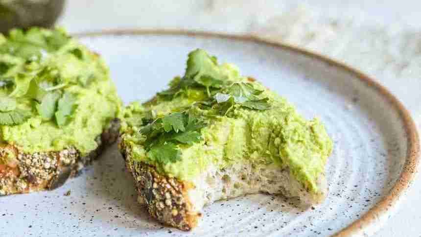 a white plate topped with a piece of bread covered in guacamole