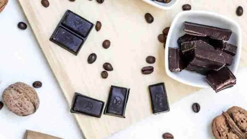 Dark chocolate and coco seeds on table near bowls
