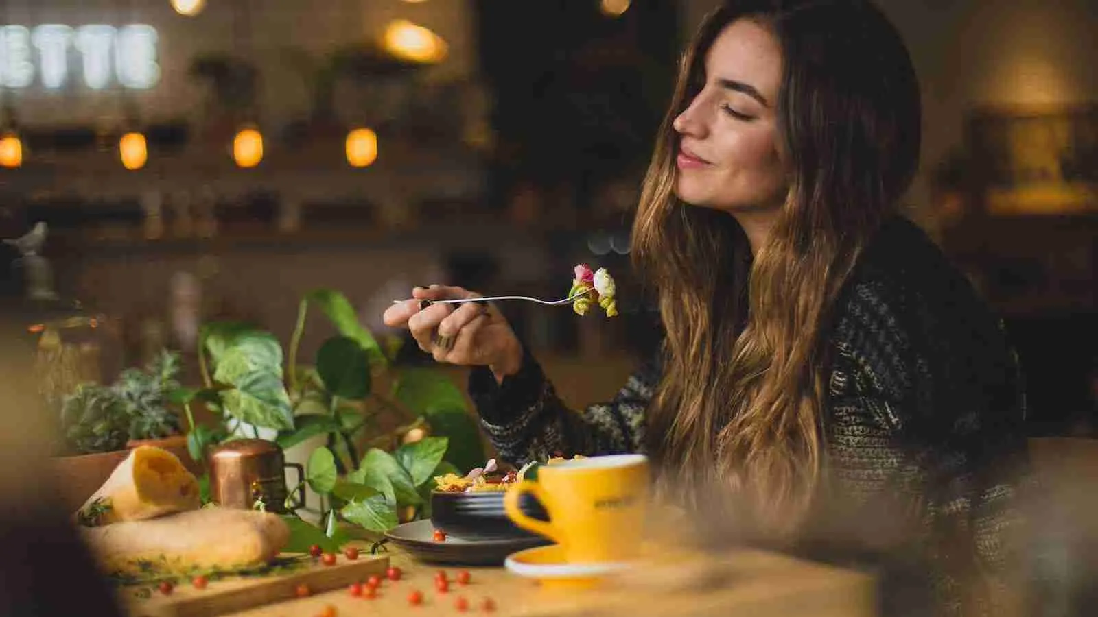 woman holding fork in front table while eating and in a delightful mood