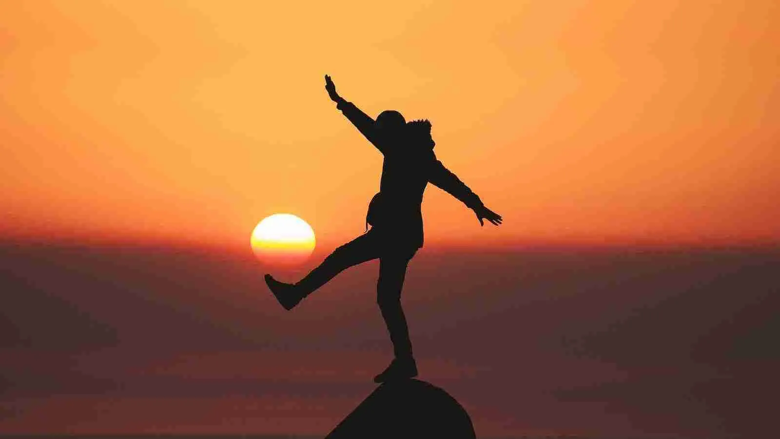 photo of silhouette photo of man standing on rock during a sunset