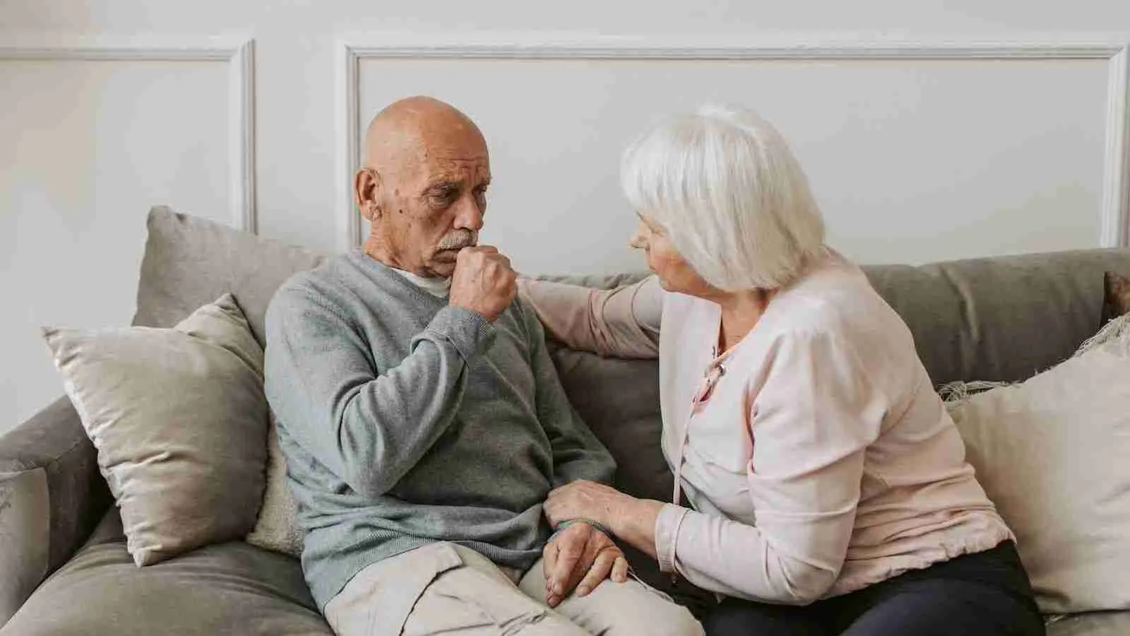 Man in Gray Sweater Sitting Beside Woman as he coughs