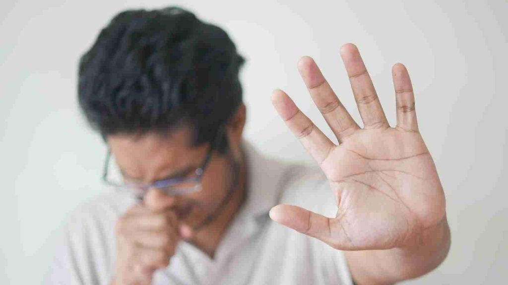 a man holding his hand up in front of his face as he coughs