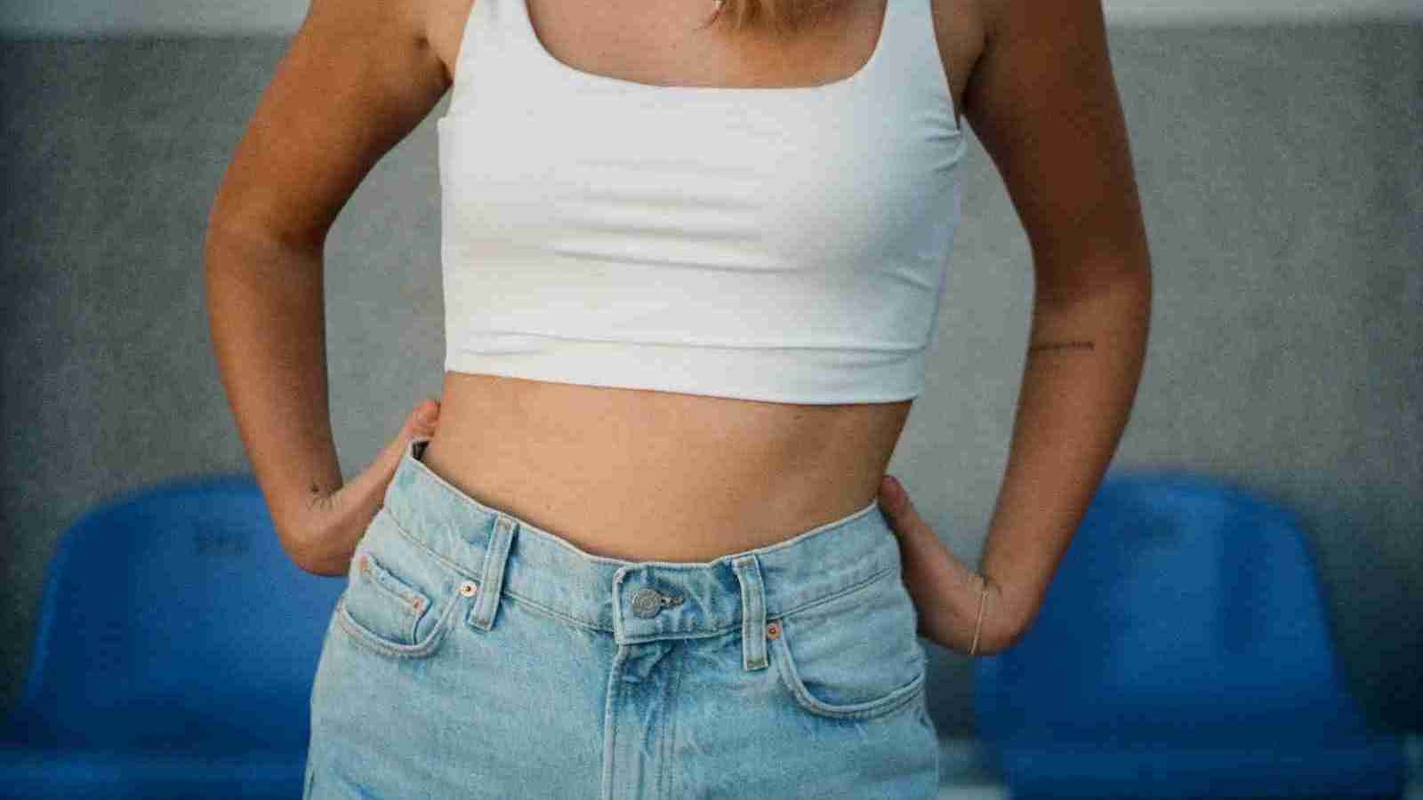 woman in a white tank top and blue denim jeans with a focus shot of her abdomen