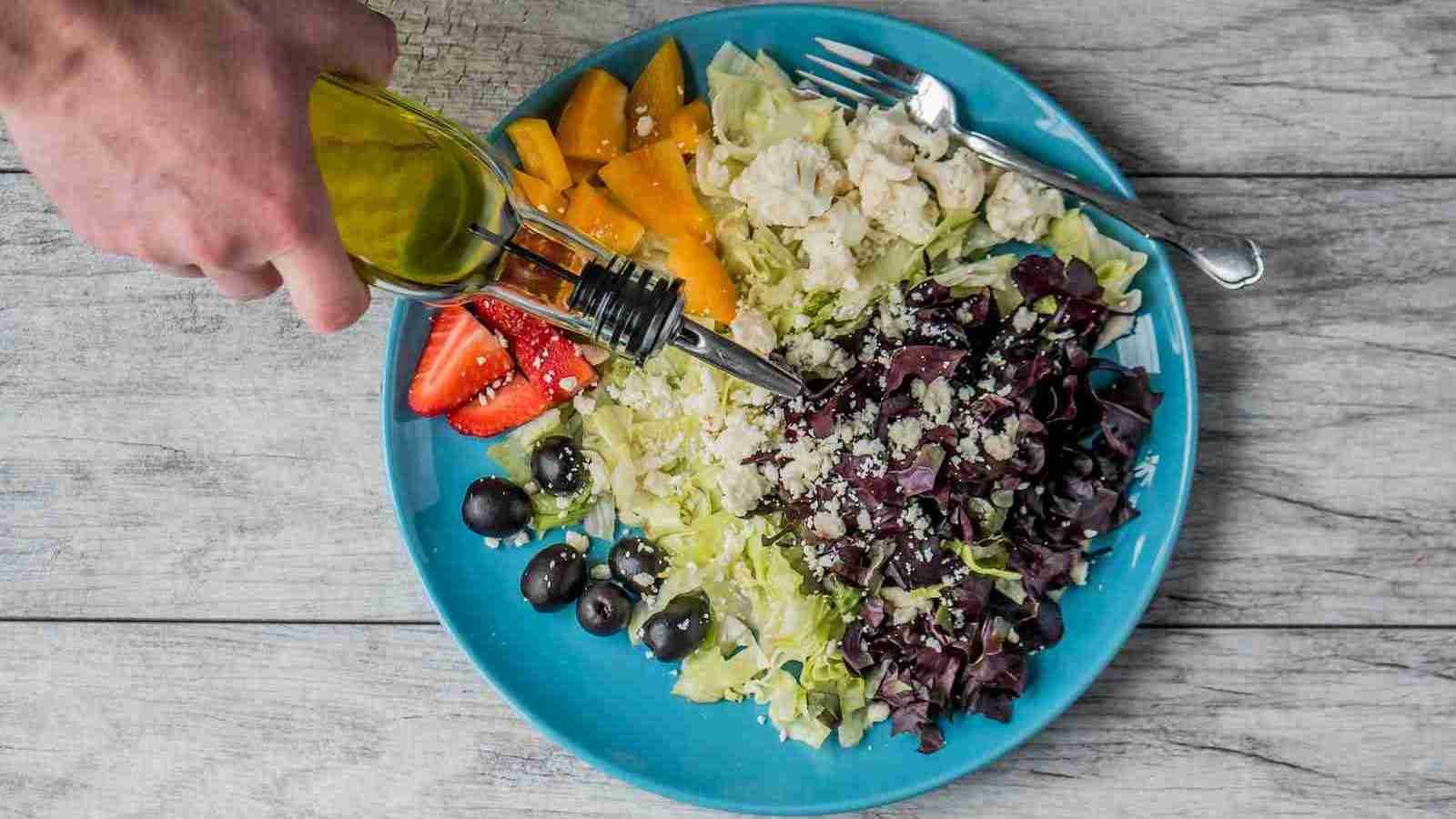 flat lay photography of man making vegetable and fruit salad pouring olive oil to salad