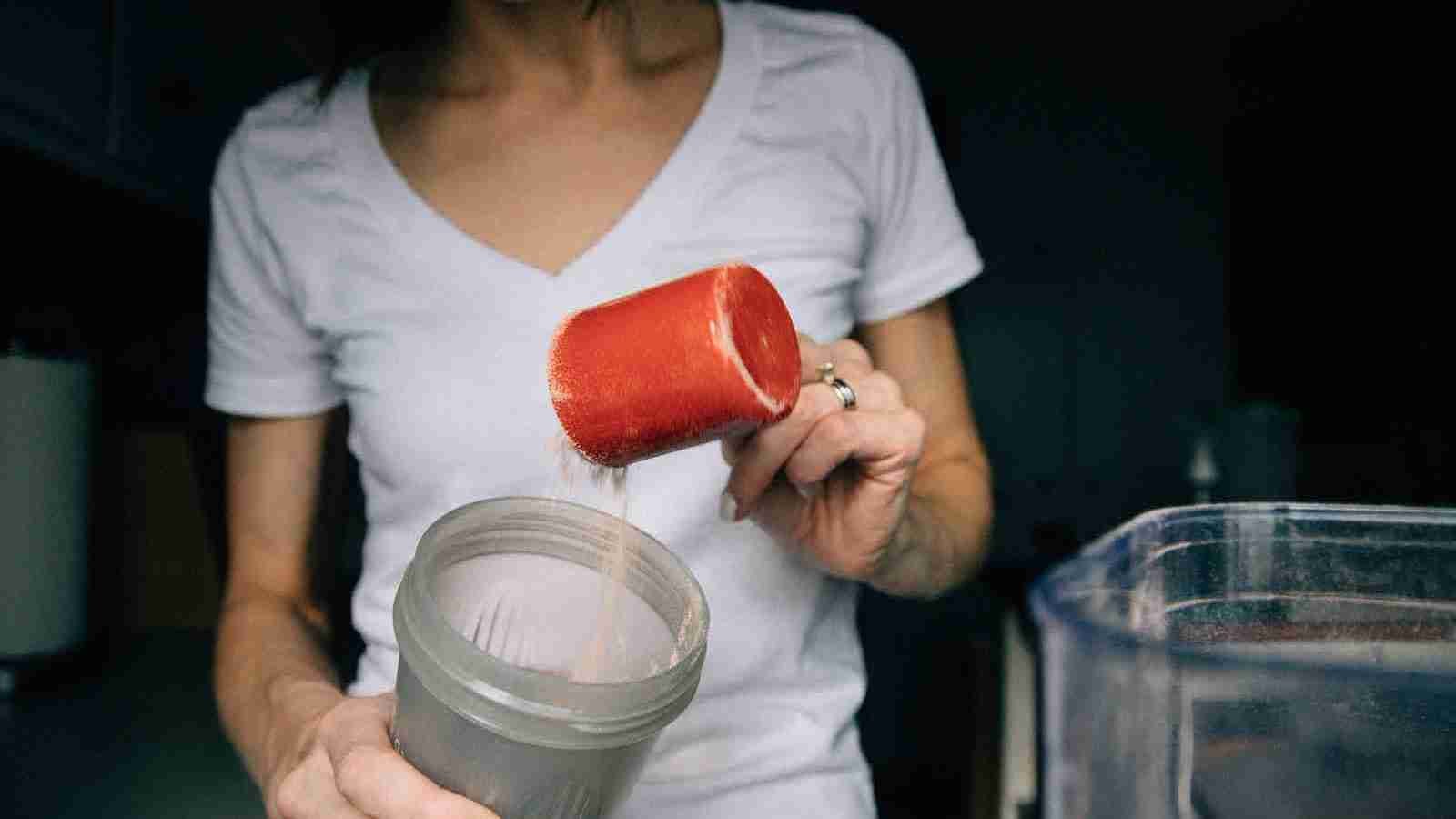 woman in white crew neck t-shirt holding red plastic cup making a protein shake