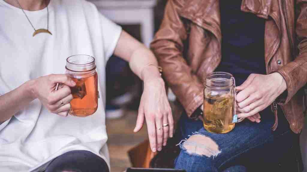 two person sitting while holding clear glass mason mugs of sweet tea