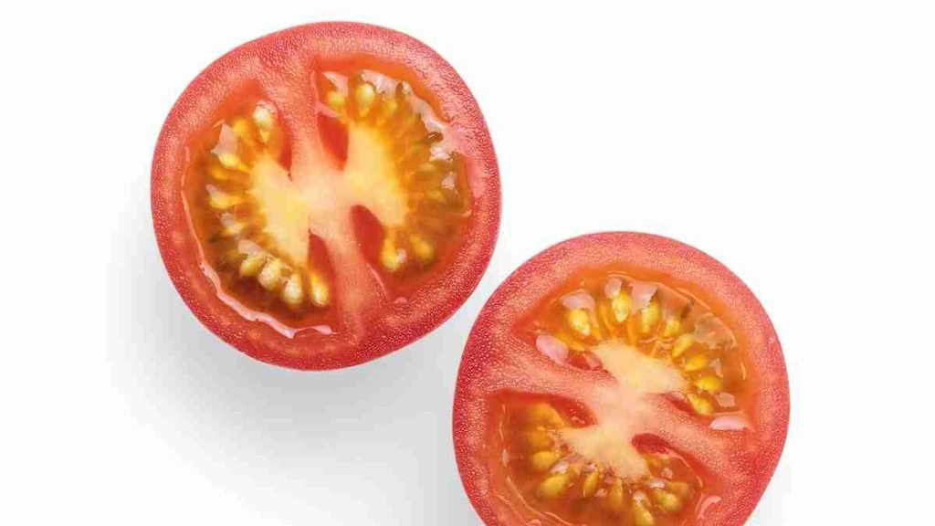 2 sliced tomato on white surface with seeds showing inside them.