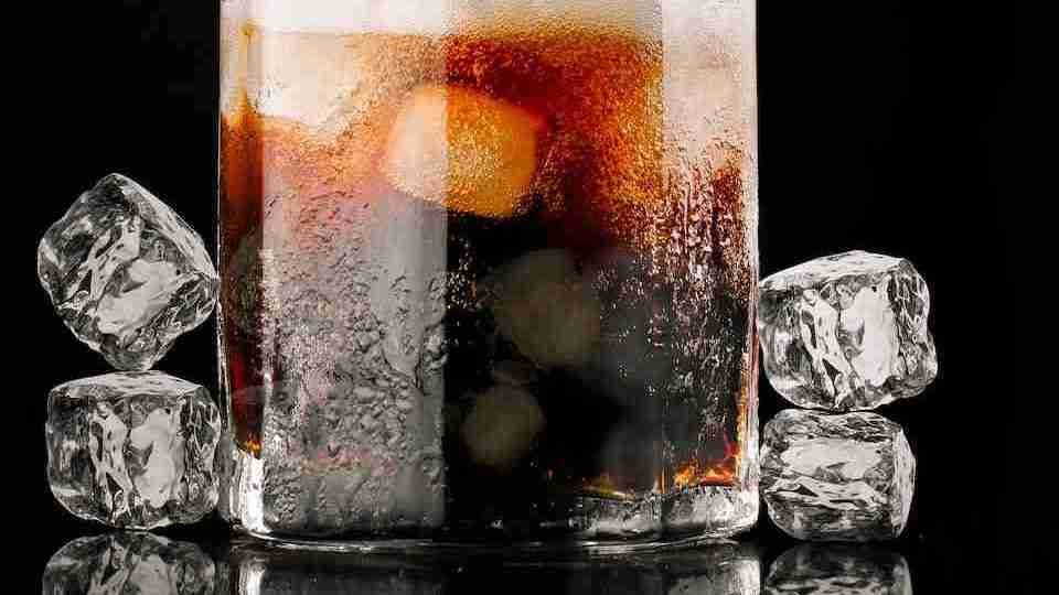 clear drinking glass with soda being poured in through a can