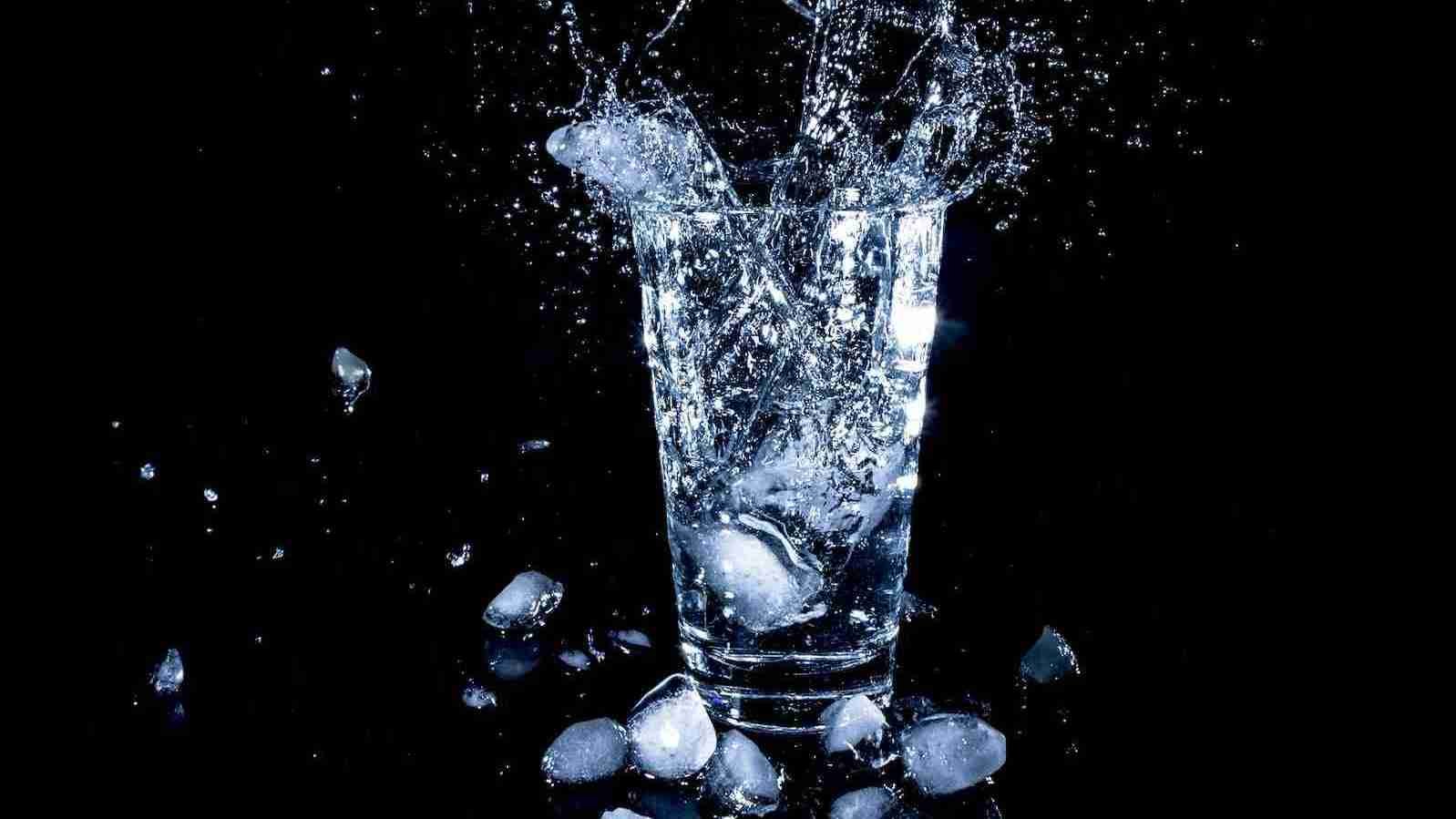ice cubes dropped in clear drinking cup with water