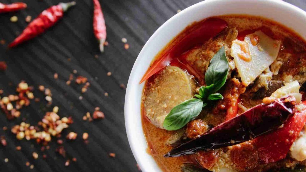 flat-lay photography of vegetable soup on white ceramic cup with red chilies on the table.