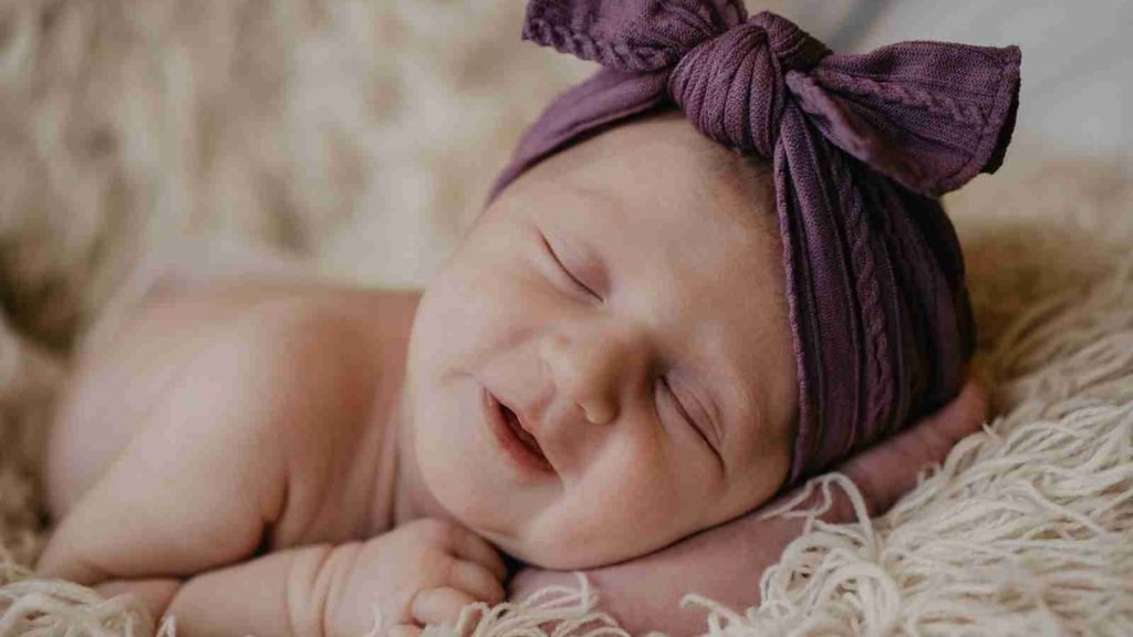 baby in purple knit cap lying on white fur textile