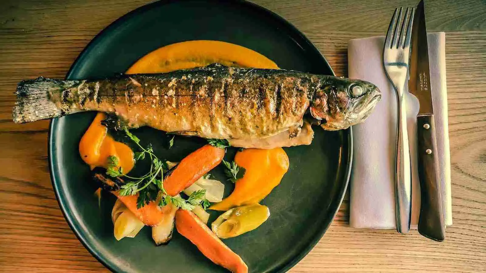 A cooked fish with vegetables on a plate
